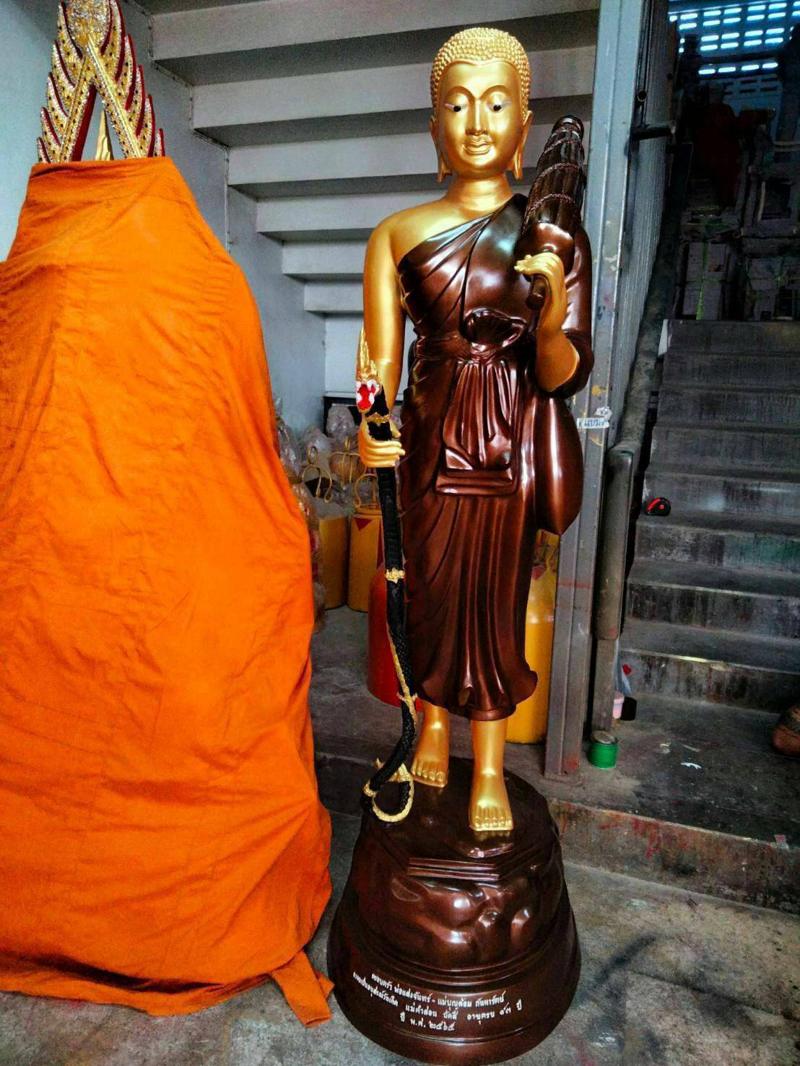 พระสีวลีสีทอง ห่มจีวรสีน้ำตาลเงา ถือไม้เท้านาคและกลด ยืนบนฐานกลม โรงหล่อพุทธบารมี